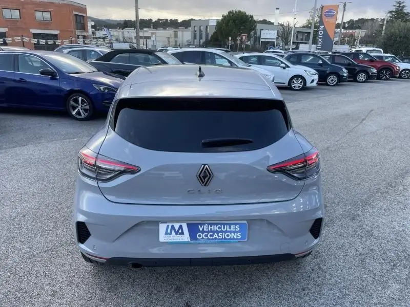 Vue arrière d'une Renault Clio V gris métal 2025, avec feux LED fins et lunette arrière teintée, sur parking extérieur.