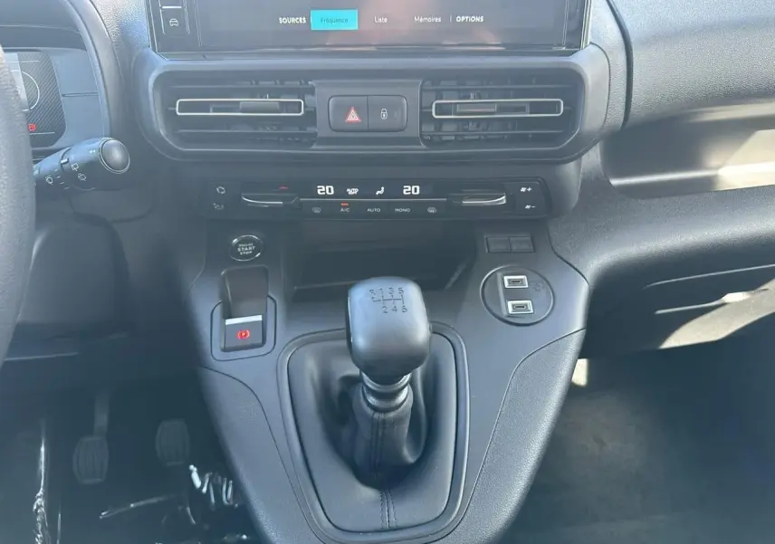 Gros plan sur la console centrale noire du Citroën Berlingo blanc, mettant en valeur le levier de vitesse manuel et l'écran tactile.