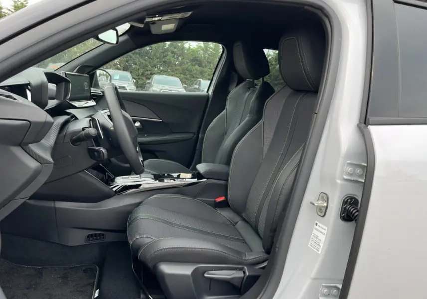 Vue intérieure côté conducteur du Peugeot 2008 Hybrid 145 GT Vision blanc okénite, sièges cuir tissu noirs avec surpiqûres vertes.