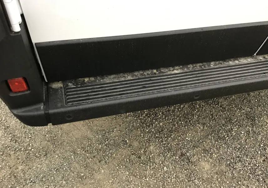 Gros plan sur la marche latérale noire du côté gauche du Peugeot Boxer Fourgon blanc, avec un feu arrière partiel visible.