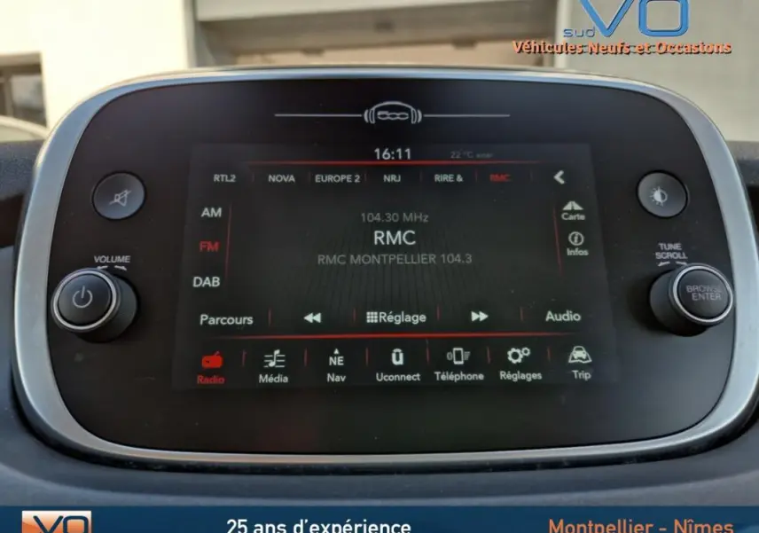 Vue de face de la console multimédia tactile du Fiat 500X gris clair, affichant la radio RMC à 104.3 MHz