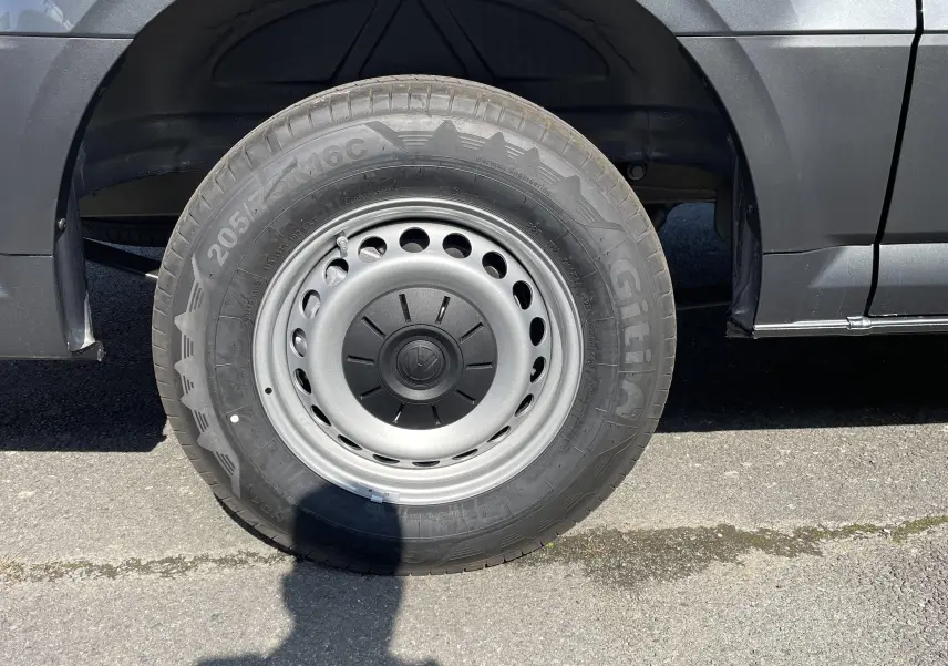 Gros plan sur la roue avant gauche du Volkswagen Crafter Van gris Indium, soulignant la jante acier et le pneu robuste.