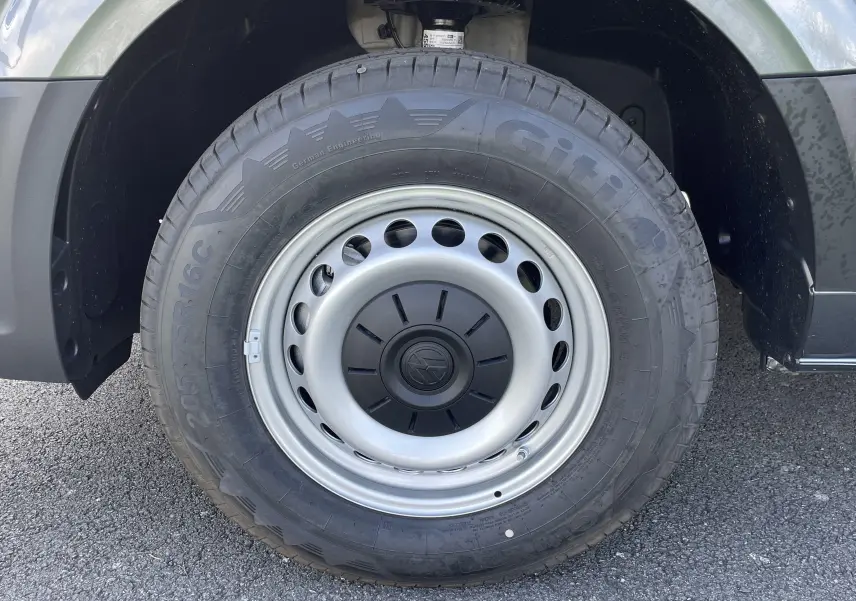 Gros plan sur la roue avant droite du Volkswagen Crafter Van gris Indium, jante acier avec logo VW central.