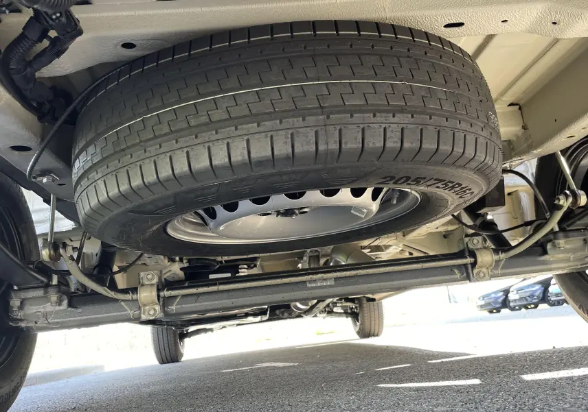 Vue en contre-plongée sous un Volkswagen Crafter gris Indium, montrant la roue de secours et le train arrière.