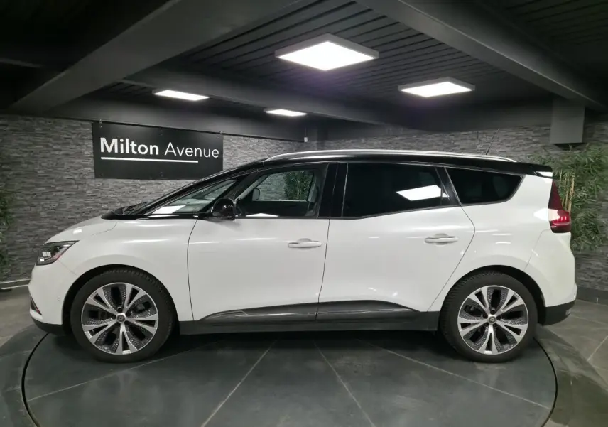 Profil droit d'un Renault Scénic blanc nacré avec toit noir et jantes alliage 20 pouces dans un showroom.