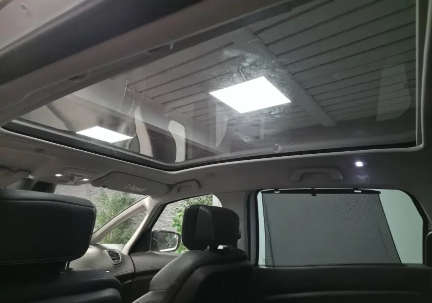 Toit panoramique en verre du Renault Scenic Grand blanc, vue intérieure arrière avec sièges cuir carbone foncé et pare-soleil.