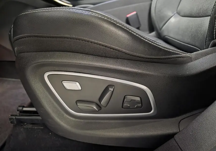 Gros plan sur les commandes électriques du siège conducteur en cuir carbone foncé du Renault Scenic blanc de 2017.