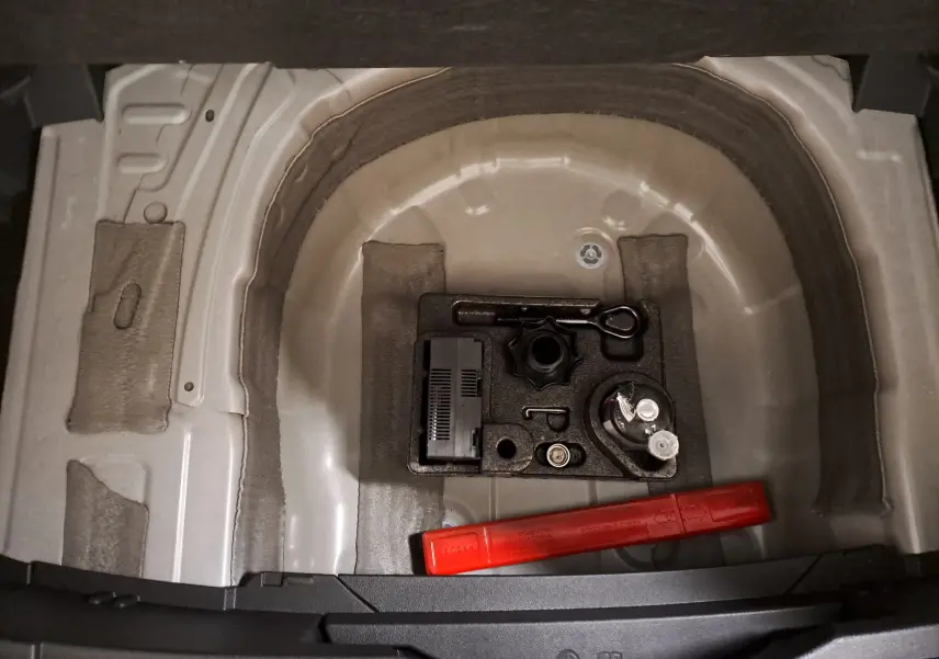 Coffre ouvert du Volkswagen T-Cross blanc, vue plongeante sur le rangement sous plancher avec outils et triangle de signalisation rouge.