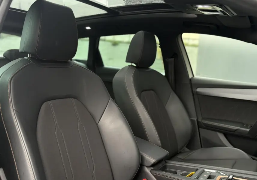 Vue intérieure avant des sièges en cuir noir du CUPRA LEON ST 2025 avec toit ouvrant panoramique visible.