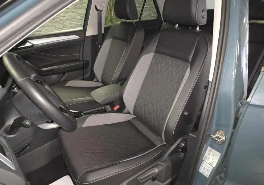 Vue intérieure côté conducteur du Volkswagen T-Roc 2025 bleu, sièges tissu noir et gris avec surpiqûres blanches.