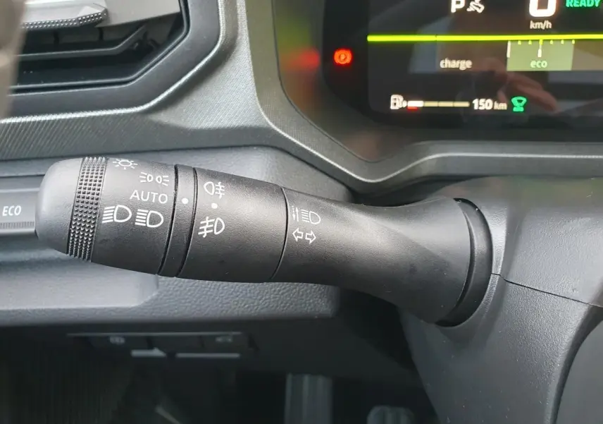 Gros plan sur la commande des feux du DACIA BIGSTER 2026, intérieur noir avec tableau de bord numérique en arrière-plan.