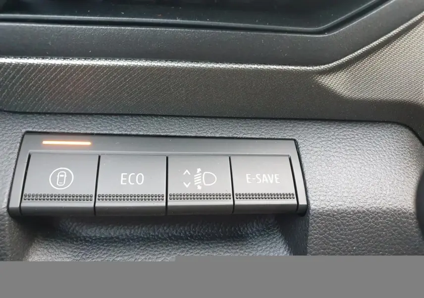 Gros plan sur les boutons de commande noirs du tableau de bord du Dacia Bigster, avec témoin lumineux orange allumé.