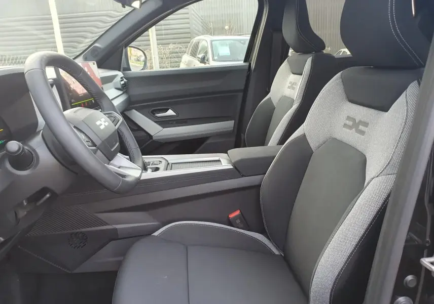 Vue intérieure côté conducteur du Dacia Bigster 2026, sièges bi-matière gris et noir avec logo brodé.