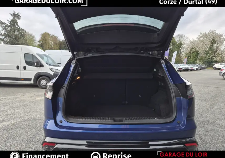 Vue arrière avec coffre ouvert d'une Renault Austral bleu foncé, stationnée en extérieur sur parking.