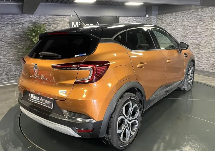 Vue 3/4 arrière droite du Renault Captur 1.6 E-Tech hybride rechargeable orange avec toit noir et jantes alliage 18 pouces.