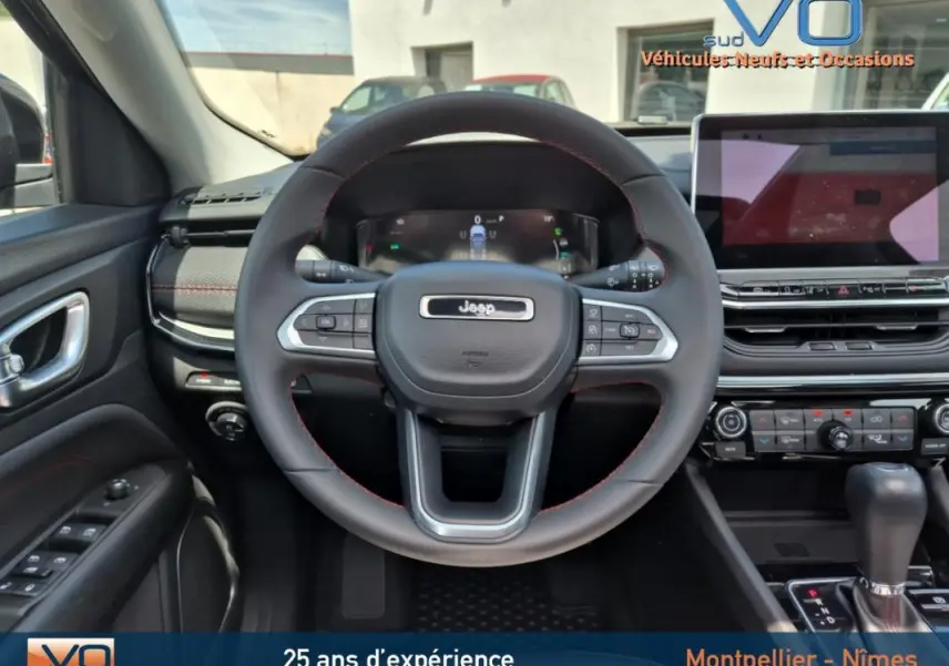 Vue intérieure centrée sur le volant du Jeep Compass gris foncé 2022 avec tableau de bord numérique et écran tactile.