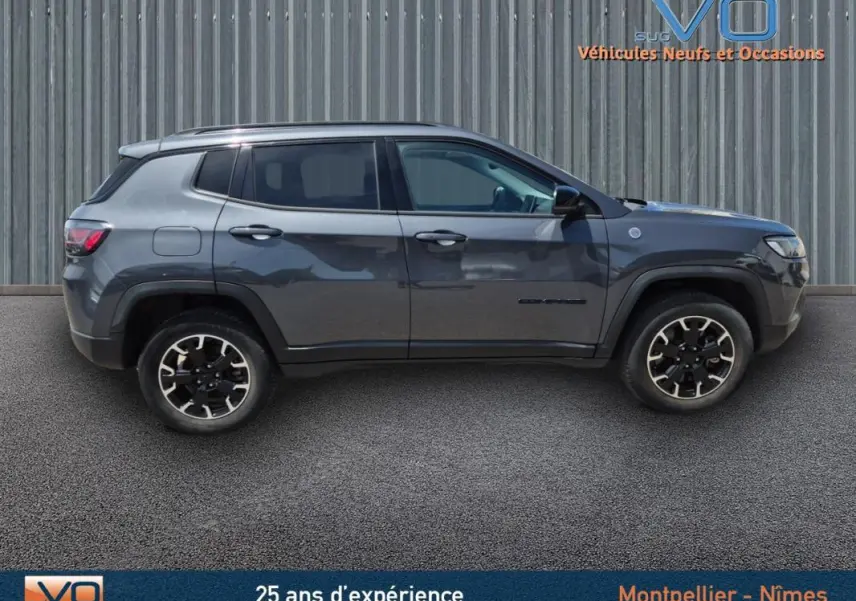 Profil côté gauche du Jeep Compass gris foncé 2022 Trailhawk hybride essence, mettant en valeur ses jantes distinctives.
