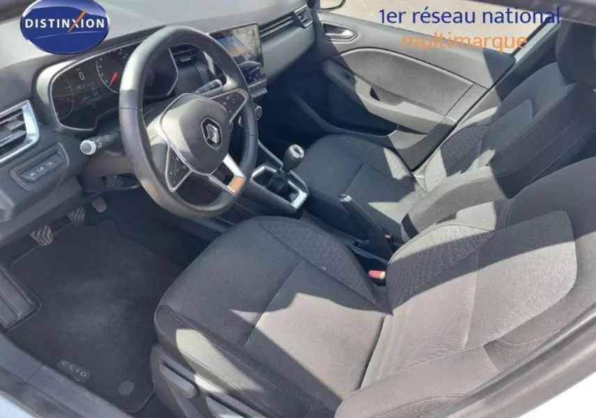 Vue intérieure côté conducteur de la Renault Clio blanche 2021, montrant le volant, la boîte manuelle et les sièges en tissu noir.