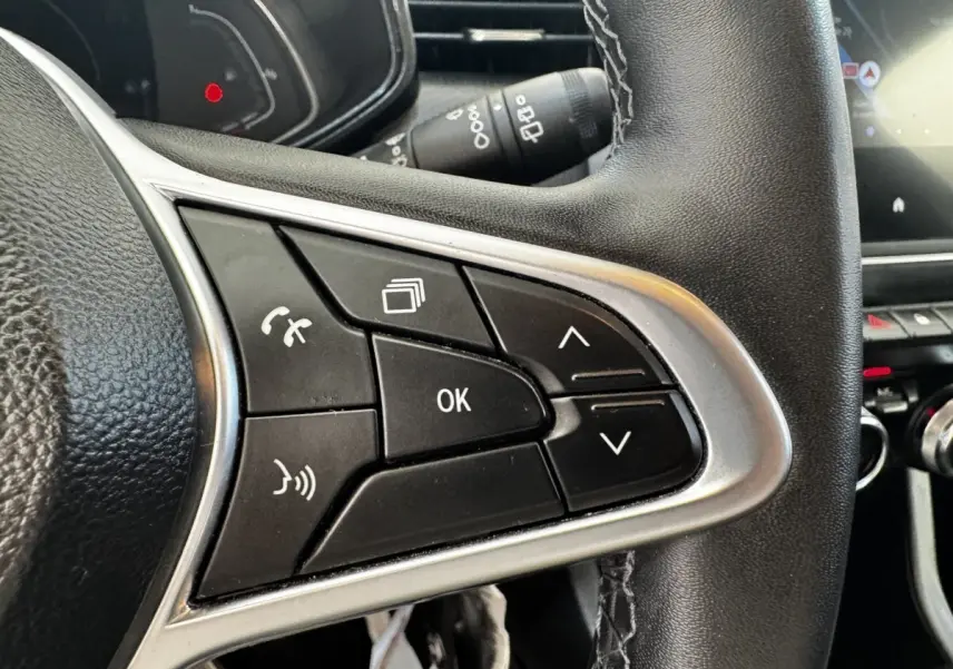 Gros plan sur les commandes multifonctions du volant cuir noir de la Renault Clio Business E-TECH 140 gris clair.