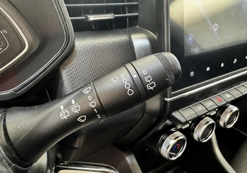 Gros plan sur la commande d’essuie-glace noire et le tableau de bord avec écran tactile dans une Renault Clio Business E-TECH gris clair.