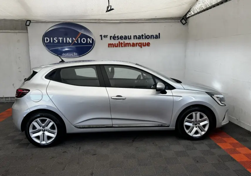 Profil côté gauche d'une Renault Clio Business E-TECH 140 gris clair, avec jantes alliage et toit spoiler visible en intérieur showroom.