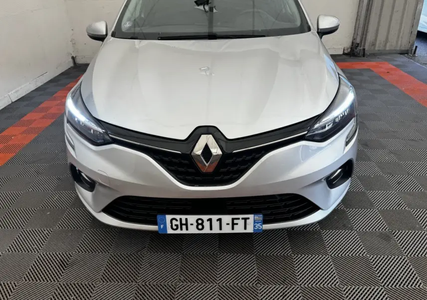Vue de face d'une Renault Clio Business E-TECH 140 gris clair avec phares LED allumés sur sol à damier noir et orange.