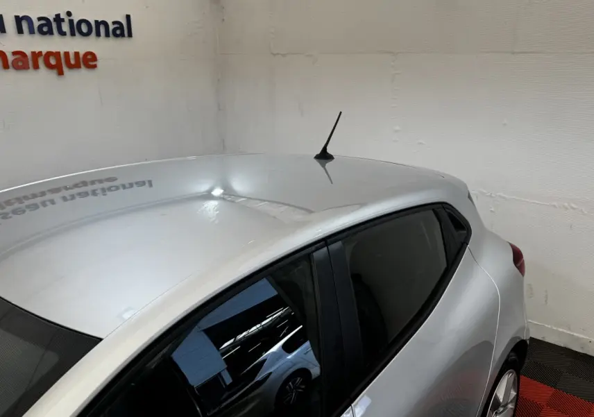 Vue 3/4 arrière droite d'une Renault Clio Business E-TECH 140 gris clair en intérieur avec toit et antenne visibles.