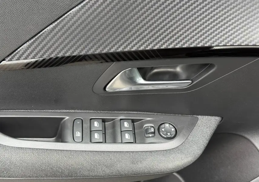 Détail de la porte avant gauche intérieure de la Peugeot 208 noire avec commandes des vitres et poignée argentée.