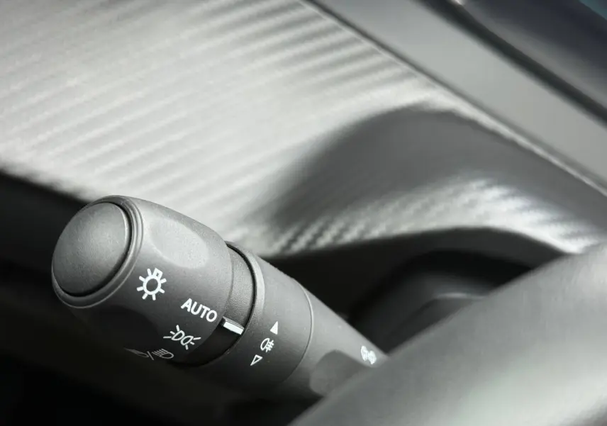 Gros plan sur la commande des phares automatique dans l'habitacle d'une Peugeot 208 noire Perla Nera.