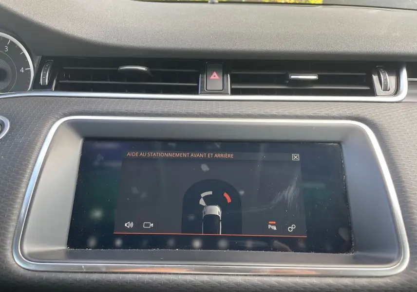 Écran tactile central du Range Rover Evoque blanc 2020 montrant l'aide au stationnement avant et arrière.
