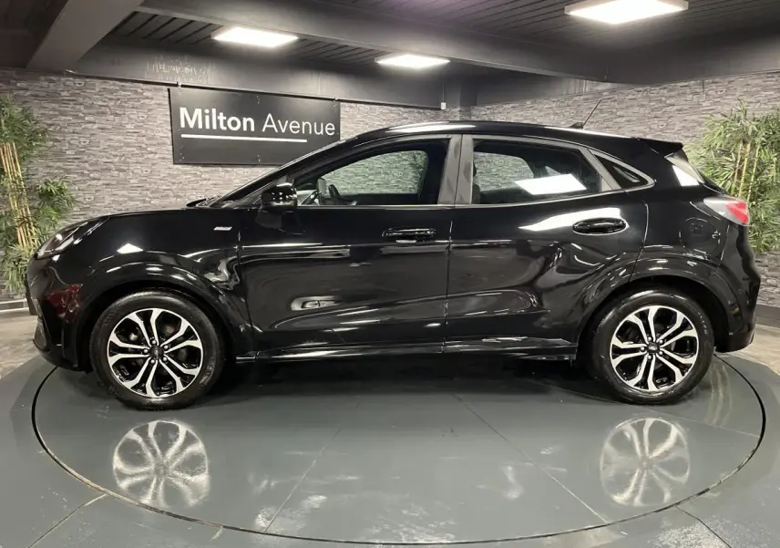 Ford Puma noir vue de profil côté gauche avec jantes alliage bicolores et toit noir brillant en intérieur showroom