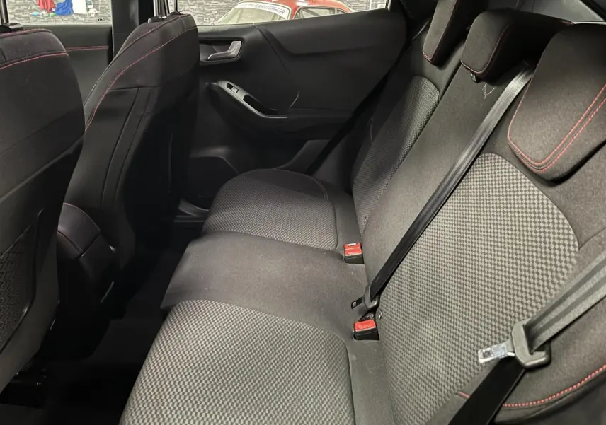 Vue intérieure côté droit de la banquette arrière noire du Ford Puma 2023 avec surpiqûres rouges et ceintures de sécurité.