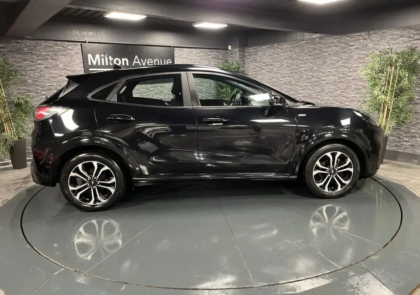 Ford Puma noir vue de profil côté gauche, avec jantes alliage noires et détails brillants en intérieur showroom.