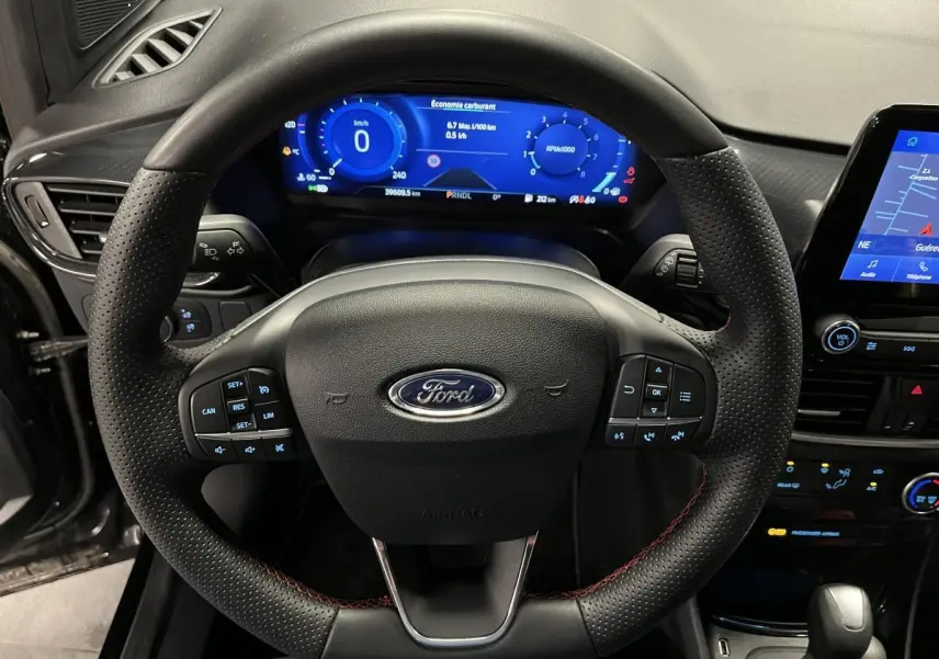 Vue rapprochée du volant noir perforé avec surpiqûres rouges et tableau de bord numérique bleu du Ford Puma 2023.