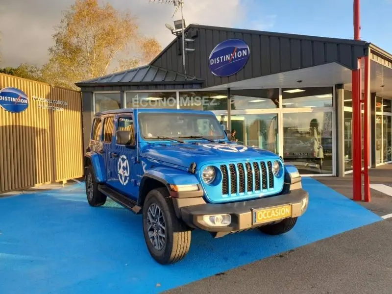 Jeep Wrangler 2.0 T 380ch 4xe Sahara Command-Trac bleu Hydro Blue vue 3/4 avant sur parking devant concession Distinxion