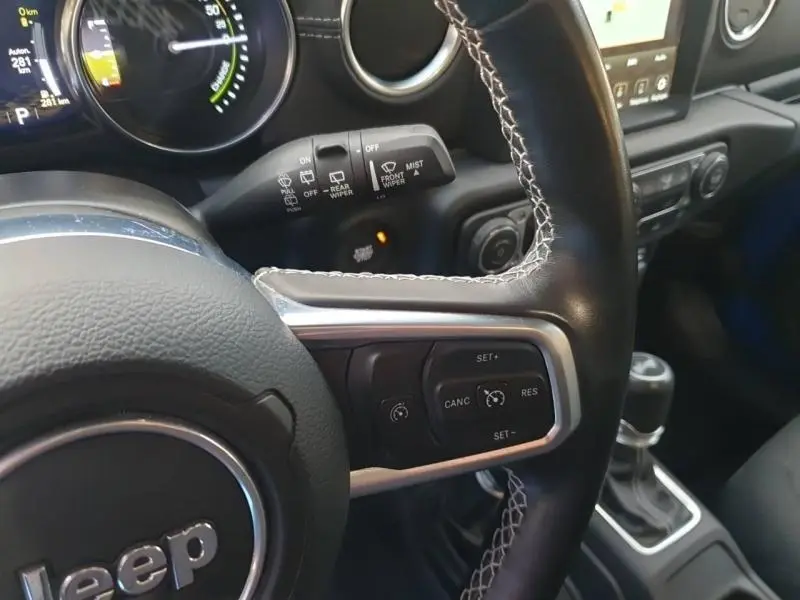 Gros plan sur le volant en cuir noir avec commandes multifonctions du Jeep Wrangler Hydro Blue, tableau de bord et levier de vitesse visibles.