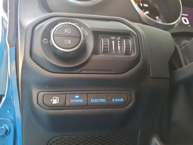 Détail du tableau de bord côté gauche d'une Jeep Wrangler Hydro Blue, avec commandes d'éclairage et modes hybride visibles.