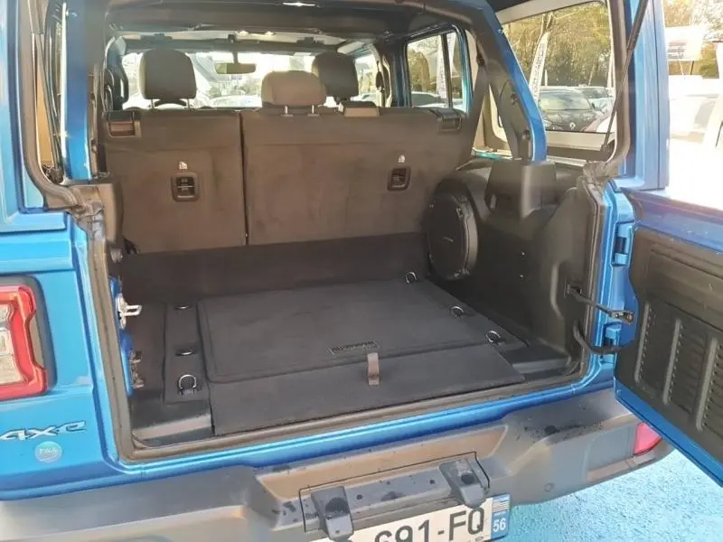 Coffre ouvert en vue arrière d'une Jeep Wrangler Sahara Hydro Blue avec intérieur noir et enceinte intégrée.