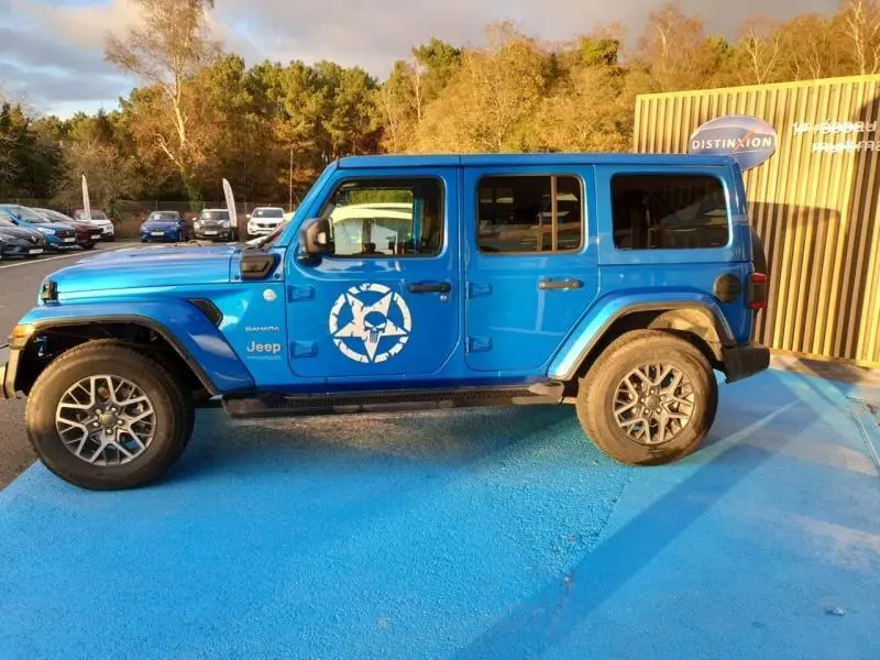 Profil gauche d'un Jeep Wrangler Hydro Blue 4 portes avec logo blanc sur la porte et jantes alu en extérieur.