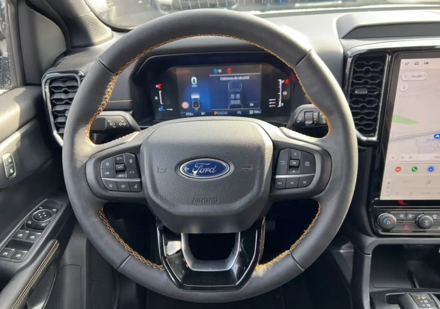 Vue intérieure centrée sur le volant cuir noir avec surpiqûres marron du Ford Ranger 2025, tableau de bord numérique et écran tactile.
