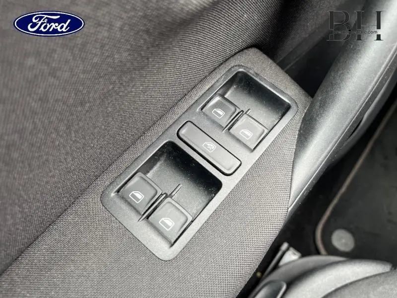 Gros plan sur les commandes électriques des vitres côté conducteur d'une Volkswagen Polo noire, intérieur tissu gris.