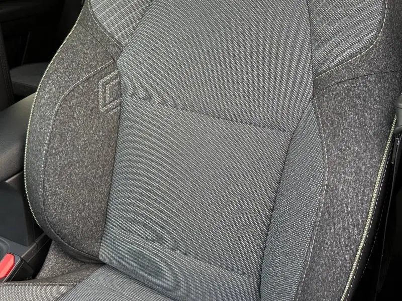 Gros plan sur le siège avant gris du Renault Captur 2025, avec surpiqûres et accoudoir central visible.