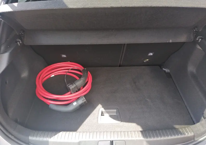 Coffre ouvert d’un Opel Mokka Electric gris, vue plongeante montrant un câble de recharge rouge enroulé.
