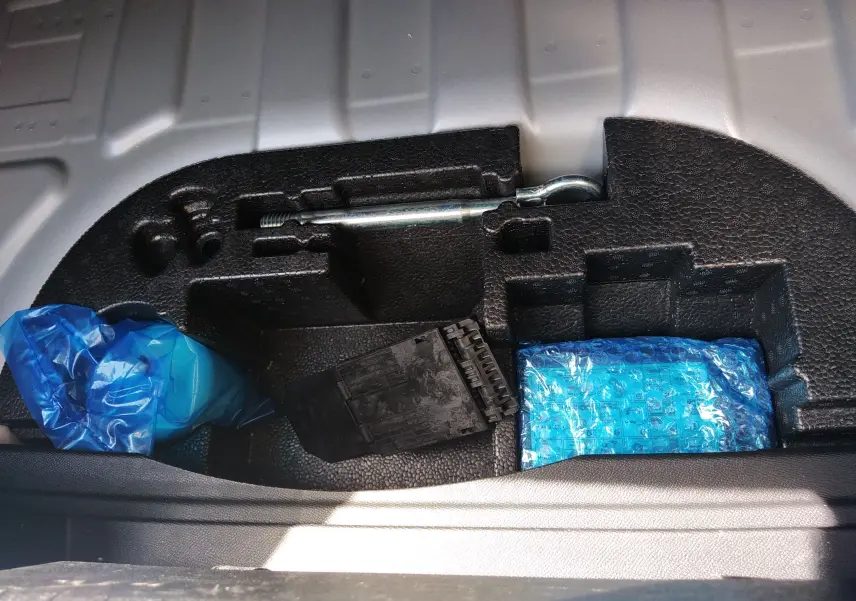 Compartiment de rangement sous le plancher de coffre d’un Opel Mokka gris, avec outils et accessoires emballés en plastique bleu.
