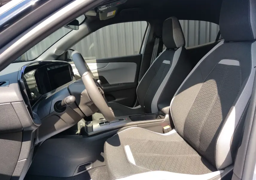 Vue intérieure côté conducteur de l'Opel Mokka Electric gris 2025, sièges tissu bicolore et tableau de bord numérique.