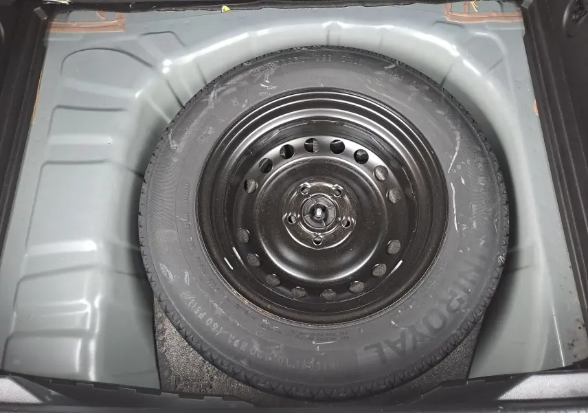 Vue plongeante sur la roue de secours noire logée dans le coffre gris clair du Renault Captur bleu marine 2022.