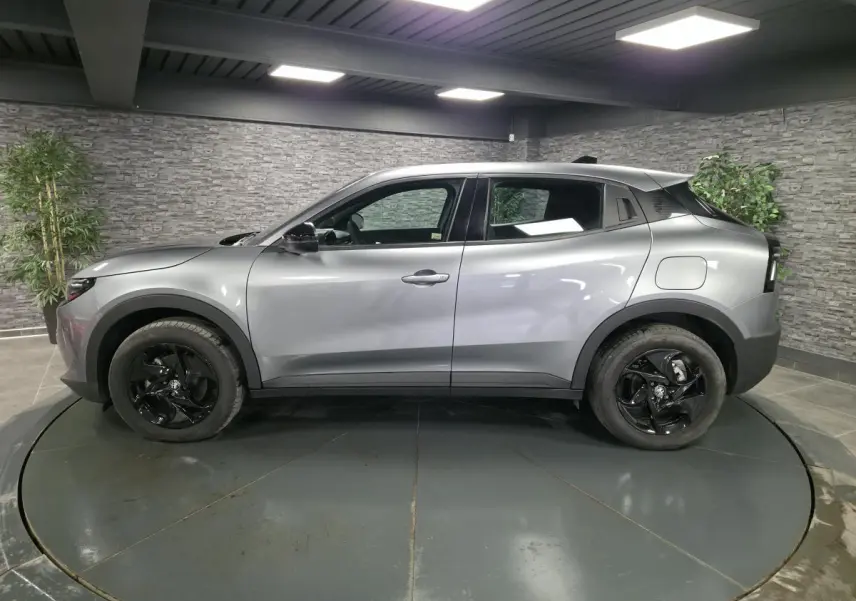 Vue de profil côté gauche d'une Alfa Romeo Junior 1.2 Ibrida grise avec jantes alliage noires dans un showroom.
