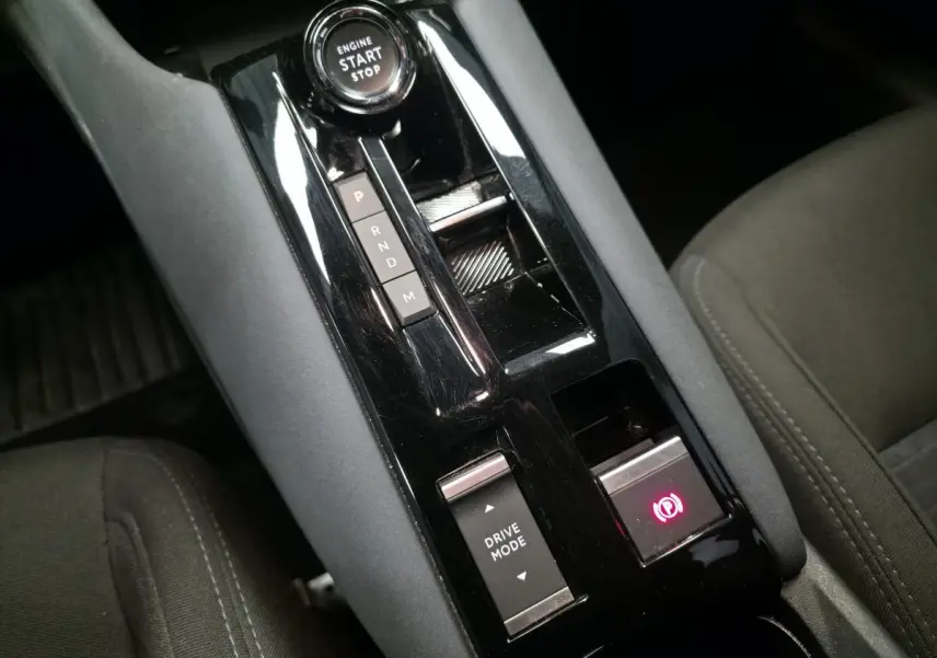 Gros plan sur la console centrale noire brillante de l'Alfa Romeo Junior 1.2 Ibrida avec sélecteur de mode de conduite et frein électrique.