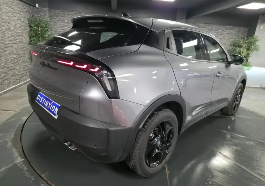 Vue 3/4 arrière droite de l'Alfa Romeo Junior 1.2 Ibrida gris métallisé avec jantes noires et feux arrière LED distinctifs.