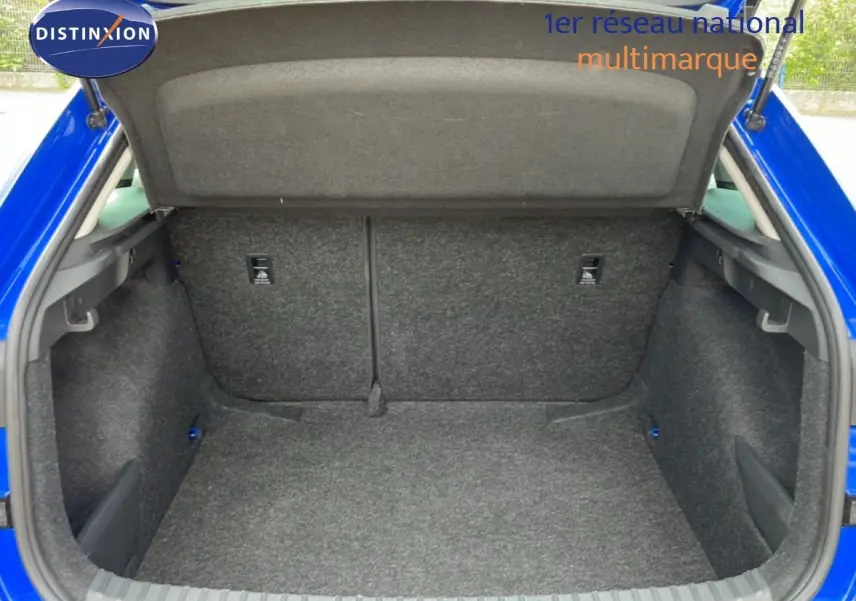 Coffre ouvert vu de l'arrière d'une Skoda Scala bleu racing metal, montrant l'espace de chargement vide et la moquette grise.